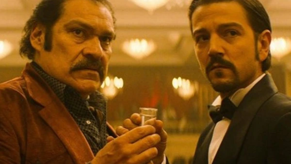 Two men toasting in a grand setting from Narcos: Mexico.