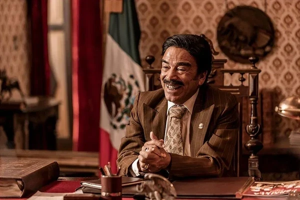 A character dressed formally, seemingly a president - like figure, smiling in ¡Que viva México!