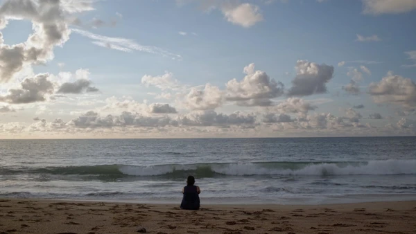 A woman sits on a beach gazing at the ocean in Los Últimos Recuerdos de Abril.